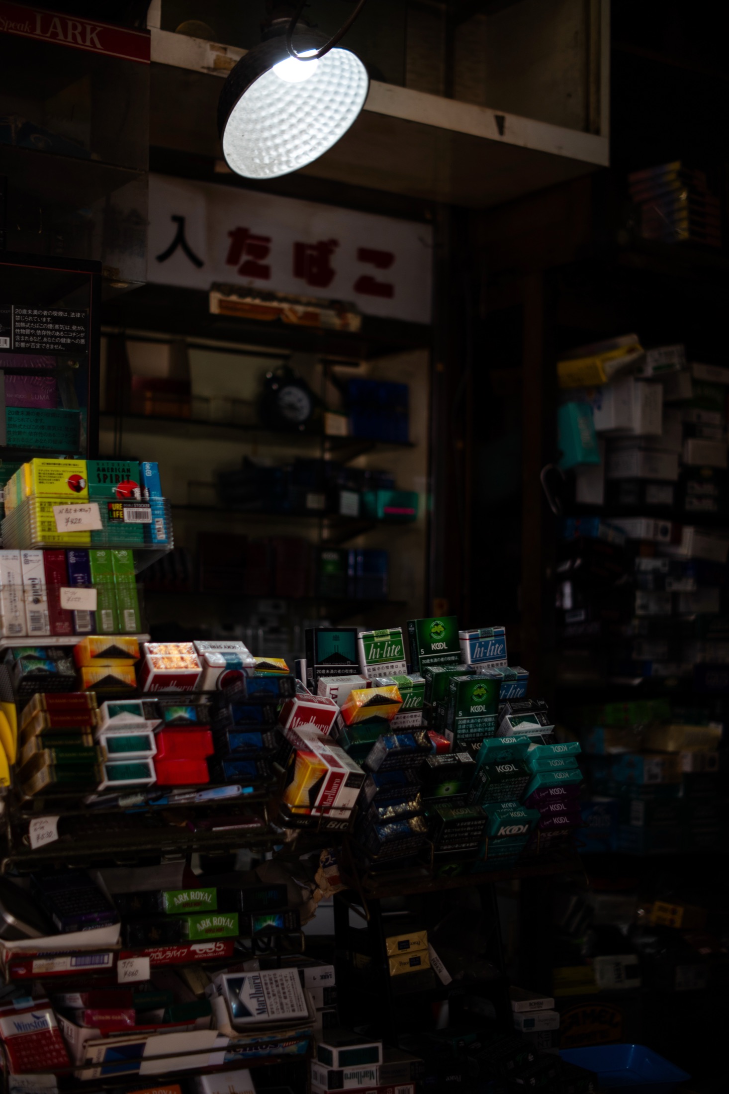 Convenience store packed with produce and boxes, warm light spilling onto the street