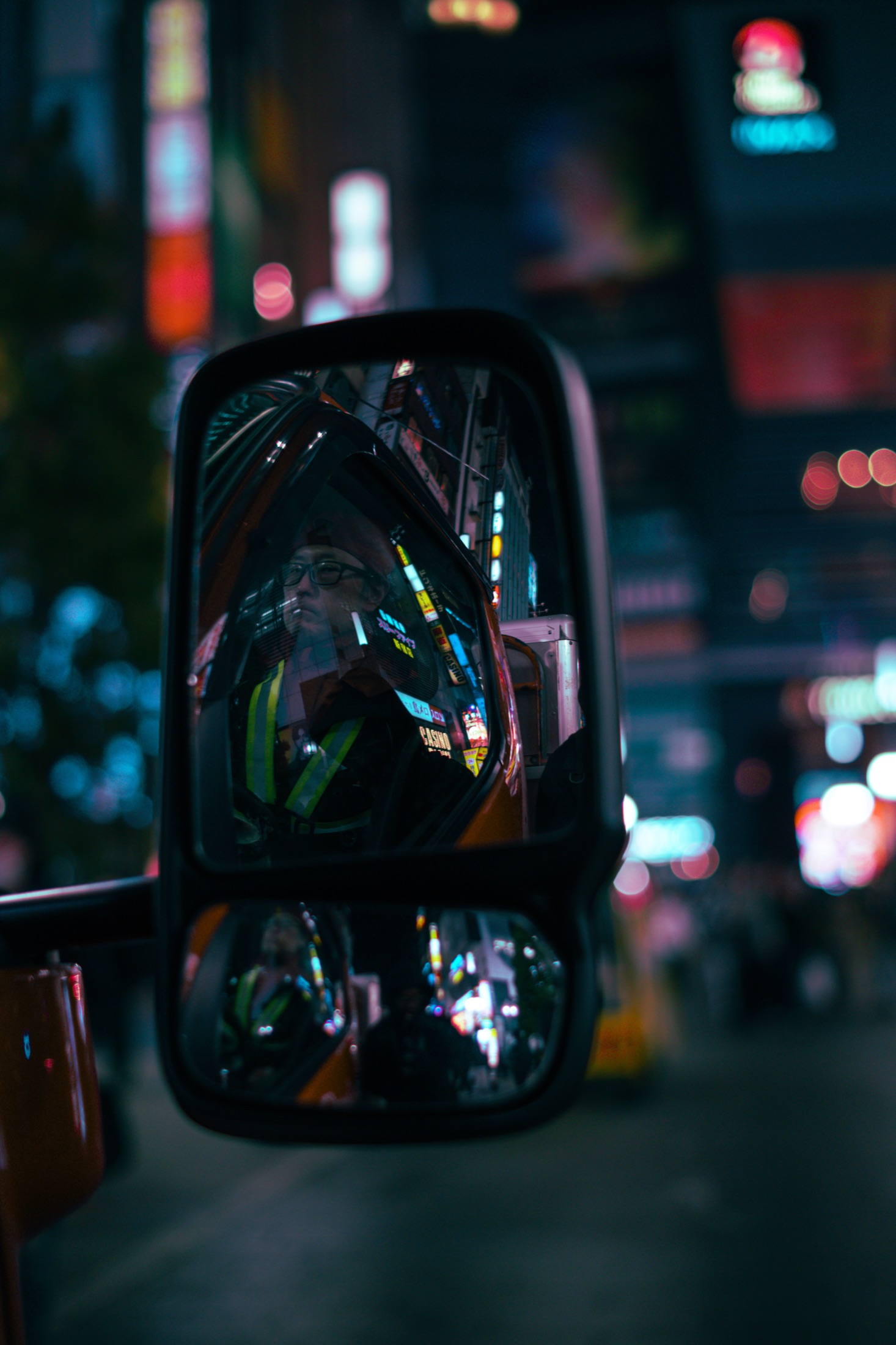 Neon reflected in a car's side mirror, city lights thrown out of focus